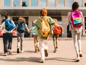 Little kids schoolchildren pupils students running hurrying to the school building for classes lessons from to the school bus. Welcome back to school. The new academic semester year start