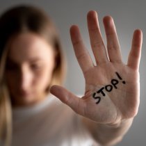 Woman with bruises on her face showing stop sign, palm in focus.