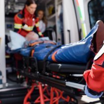 Selective focus of paramedic in uniform carrying stretcher with patient in ambulance ca outdoors