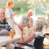 Elderly man talking with disabled woman while sitting together at table in common room